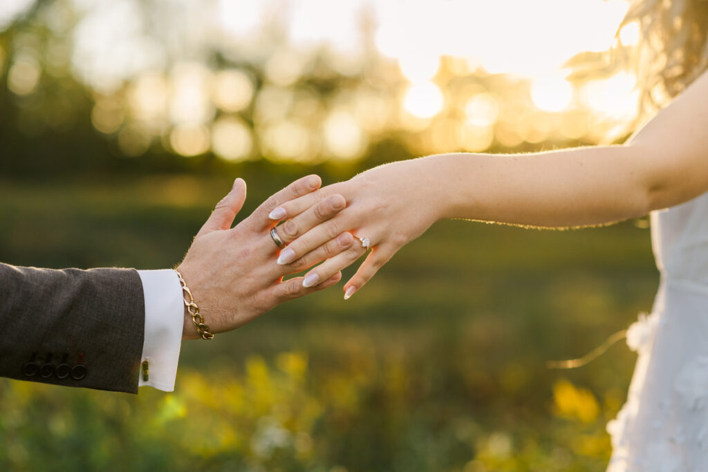 Close-up of the couple’s hands reaching out to each other, showcasing the woman’s engagement ring, with a blurred nature background.